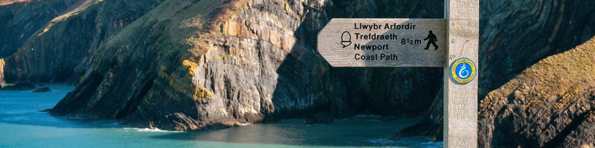 Wales Coast Path and Pembrokeshire Coast Path sign with coastline out of focus in background