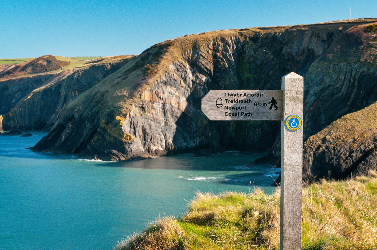 Wales Coast Path and Pembrokeshire Coast Path sign with coastline out of focus in background